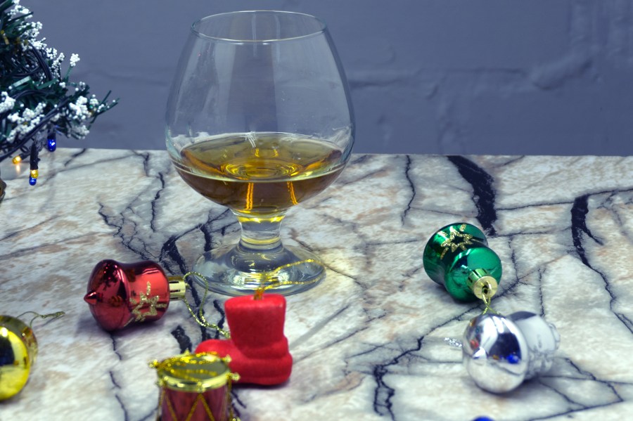 Glass of whiskey with ice, a car key and a toy car over a reindeer with lights at the