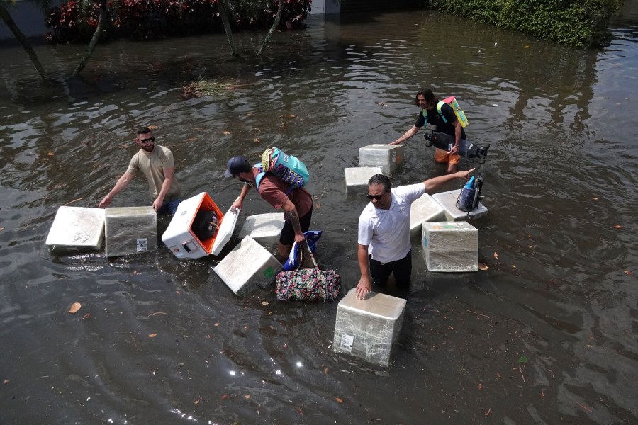 FILE - People try and save valuables as they wade through flood waters in the Edgewood neighborhood of Fort Lauderdale, Fla., April 13, 2023. Over 25 inches of rain fell in South Florida since Monday, causing widespread flooding. (Joe Cavaretta/South Florida Sun-Sentinel via AP)