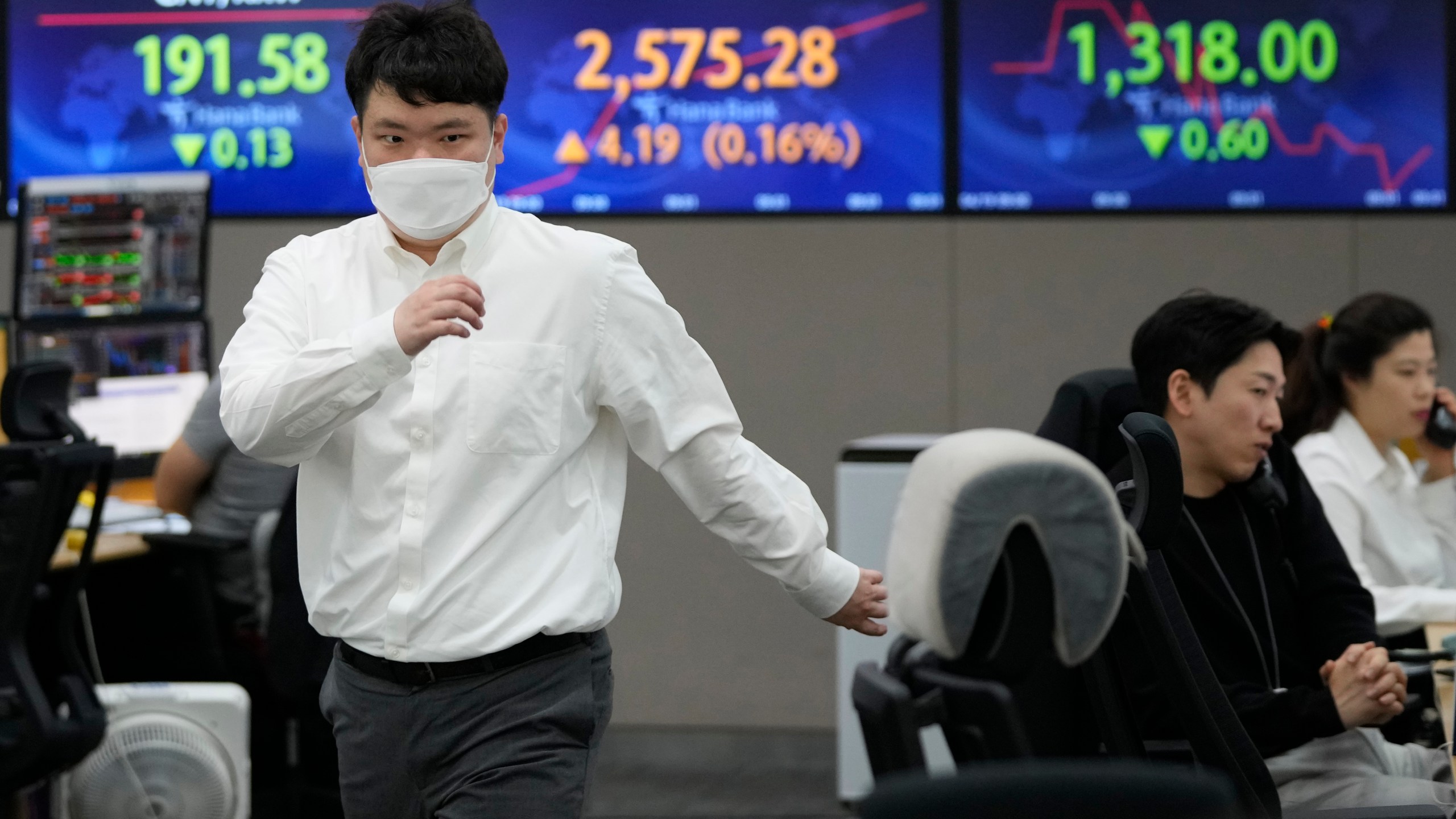 A currency trader passes by screens showing the Korea Composite Stock Price Index (KOSPI), top center, and the foreign exchange rate between U.S. dollar and South Korean won, top right, at the foreign exchange dealing room of the KEB Hana Bank headquarters in Seoul, South Korea, Wednesday, April 19, 2023. Asian shares were trading mixed Wednesday, as investors took a wait-and-see attitude ahead of earnings reports and possible moves by central banks. (AP Photo/Ahn Young-joon)