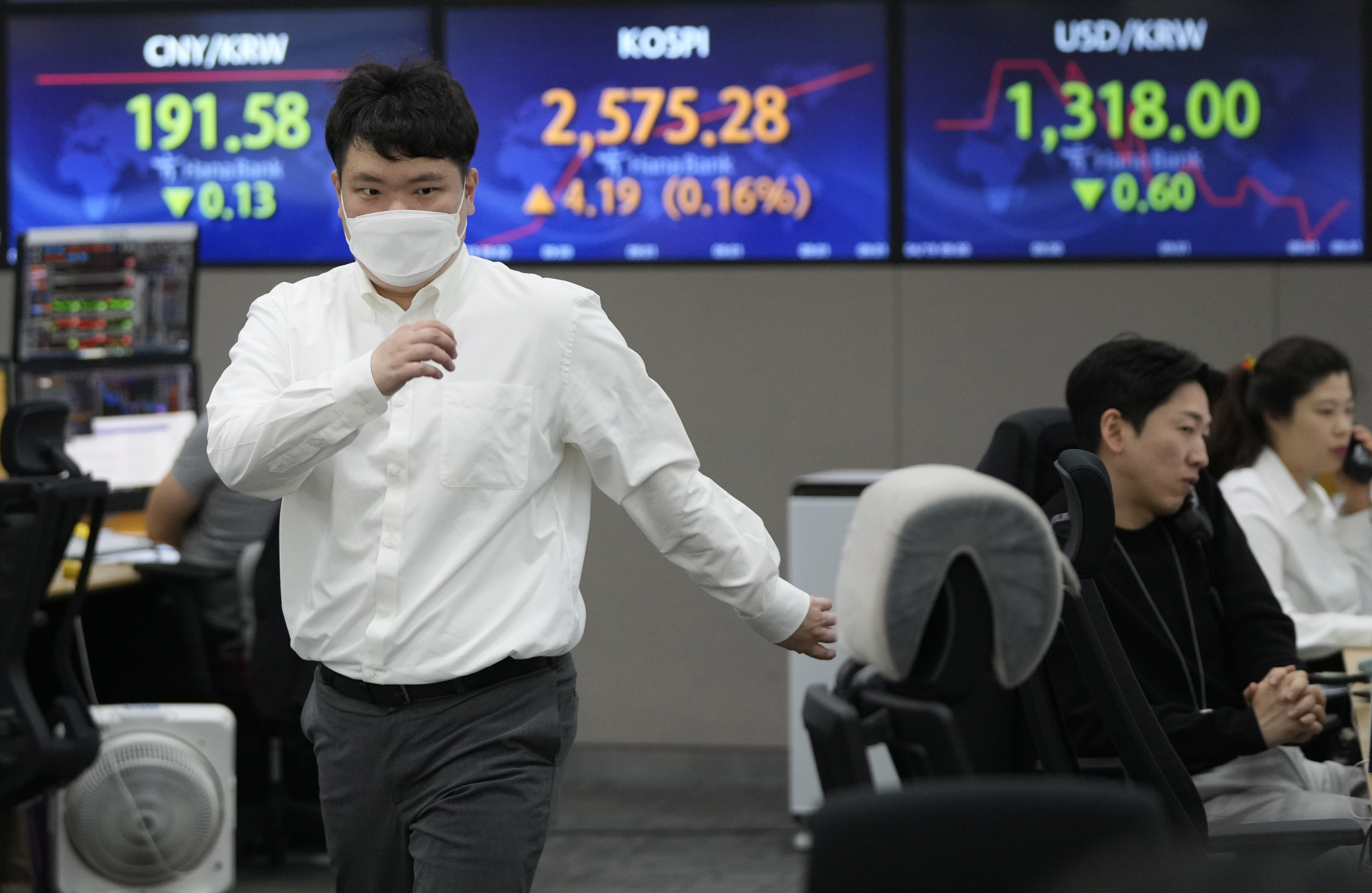 A currency trader passes by screens showing the Korea Composite Stock Price Index (KOSPI), top center, and the foreign exchange rate between U.S. dollar and South Korean won, top right, at the foreign exchange dealing room of the KEB Hana Bank headquarters in Seoul, South Korea, Wednesday, April 19, 2023. Asian shares were trading mixed Wednesday, as investors took a wait-and-see attitude ahead of earnings reports and possible moves by central banks. (AP Photo/Ahn Young-joon)