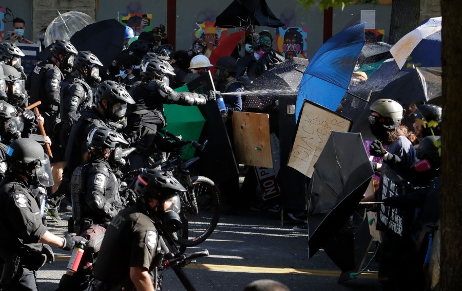 FILE - Police pepper spray Black Lives Matter protesters near Seattle Central Community College on July 25, 2020, in Seattle. The Seattle Police Department should “offer a sincere, public apology” for its violent response to people demonstrating after the Minneapolis police killing of George Floyd, a panel of police, citizens and accountability experts has concluded in a final review and report released Tuesday, April 18, 2023. (AP Photo/Ted S. Warren, File)