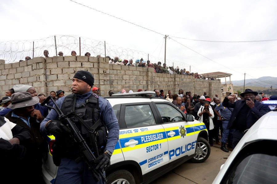 Curious onlookers behind a police cordon, where ten people from the same family were shot dead Friday, April 21, 2023. Police say 10 people were "ambushed" by unknown gunmen at a home in the city of Pietermaritzburg in the eastern KwaZulu-Natal province, South Africa. (AP Photo)