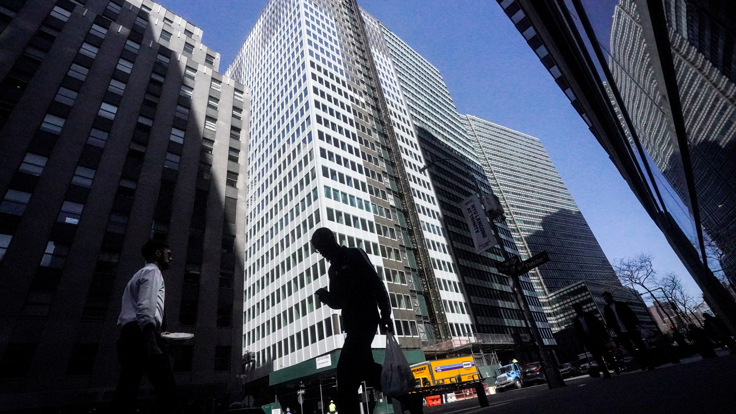 A pedestrian is silhouetted against a high rise at 160 Water Street in Manhattan's financial district, as the building is undergoing a conversion to residential apartments, Tuesday, April 11, 2023, in New York. (AP Photo/Bebeto Matthews)