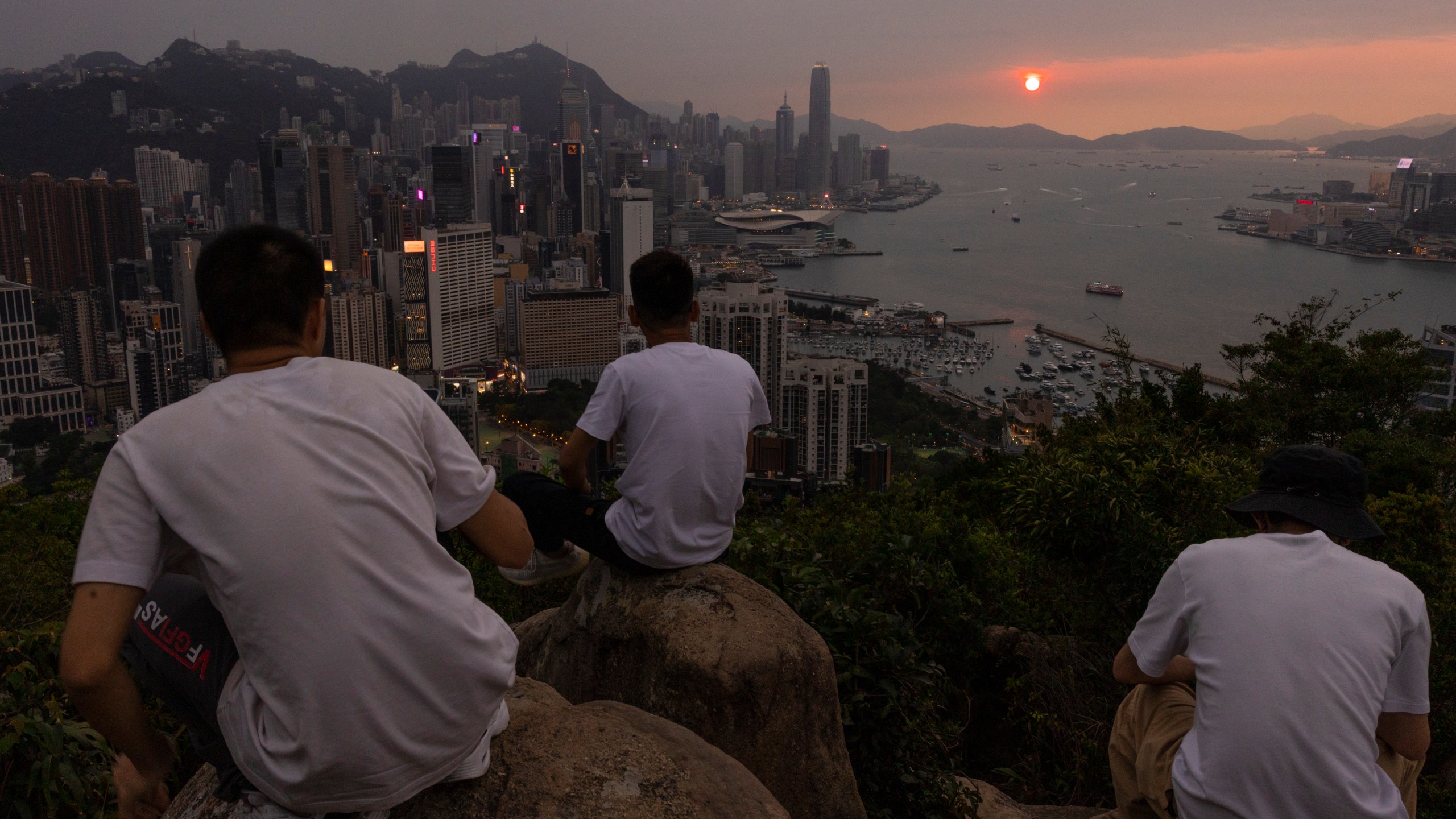 FILE - Mainland Chinese tourists look at sunset from a hill in Hong Kong, April 26, 2023. Living in Hong Kong today means juggling contradictory feelings. In 20 interviews, many said that when they focus on business indicators and everyday life, they see a recovery gathering pace after years of travel restrictions. But when it comes to anything political, the openness and freedoms that were once hallmarks of the Chinese-ruled former British colony seem permanently gone. (AP Photo/Louise Delmotte, File)