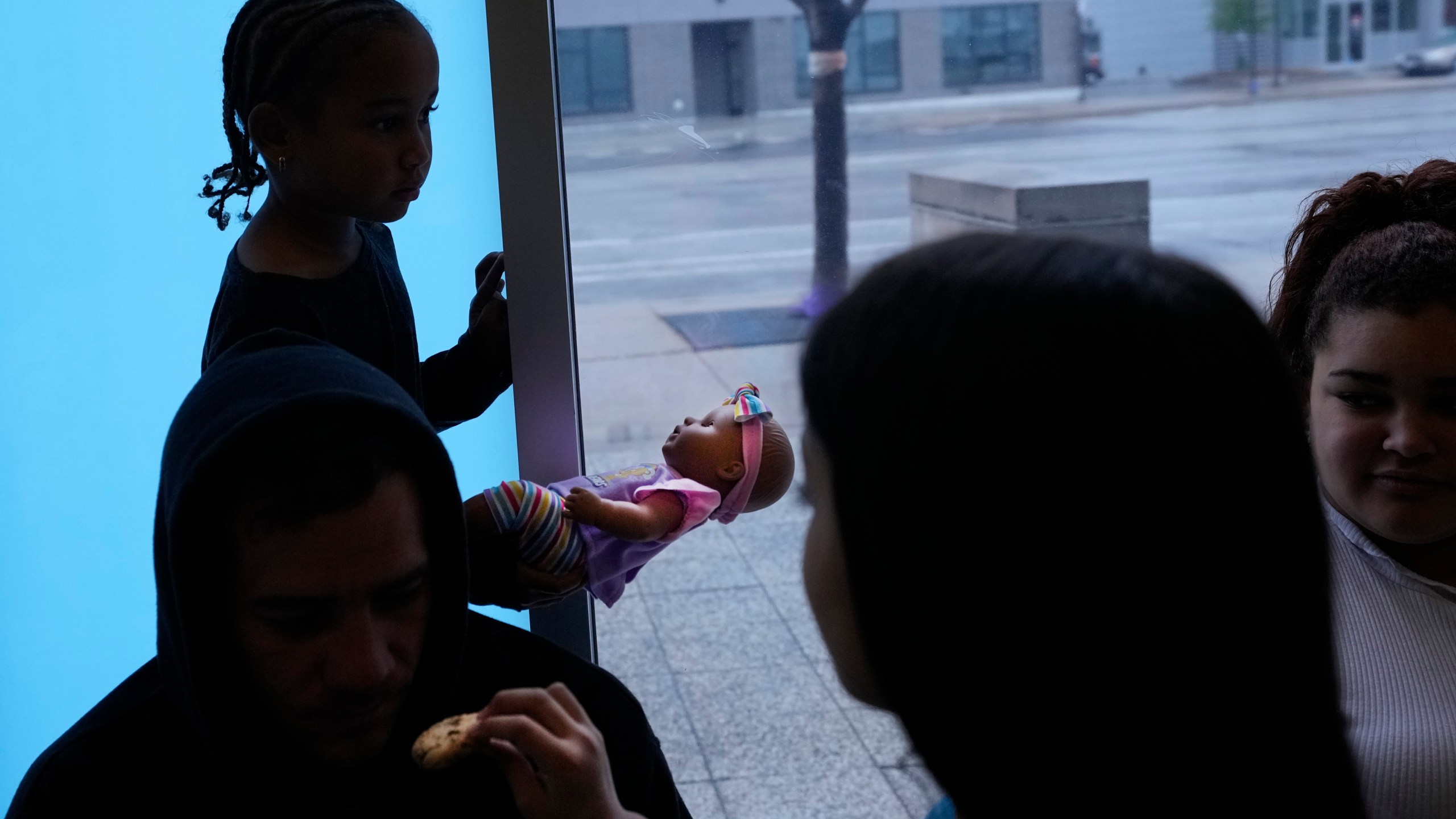 Charlotte, a Venezuelan immigrant, stands in silhouette holding a baby doll as her family and others take shelter in the Chicago Police Department's 16th District station on Monday, May 1, 2023. Chicago has seen the number of new arrivals grow tenfold in recent days. Shelter space is scarce and migrants awaiting a bed are sleeping on floors in police stations and airports. (AP Photo/Charles Rex Arbogast)