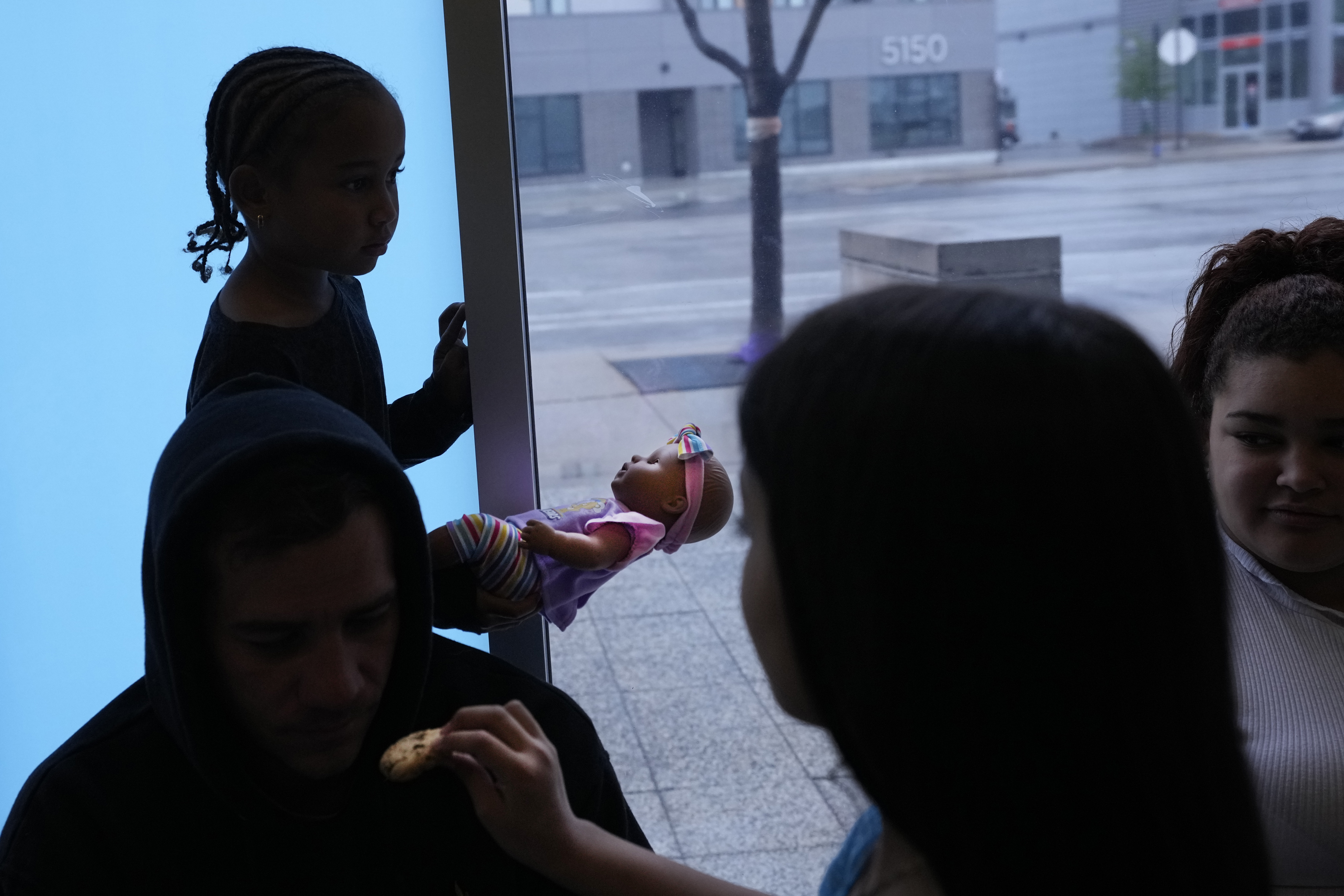 Charlotte, a Venezuelan immigrant, stands in silhouette holding a baby doll as her family and others take shelter in the Chicago Police Department's 16th District station on Monday, May 1, 2023. Chicago has seen the number of new arrivals grow tenfold in recent days. Shelter space is scarce and migrants awaiting a bed are sleeping on floors in police stations and airports. (AP Photo/Charles Rex Arbogast)