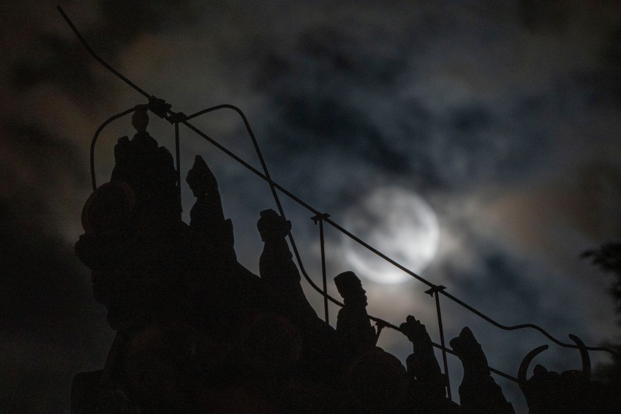 Roof decorations depicting mythical sacred beasts are silhouetted near a penumbral lunar eclipse partially blocked by clouds during the early hours of Saturday, May 6, 2023 in Beijing. (AP Photo/Ng Han Guan)