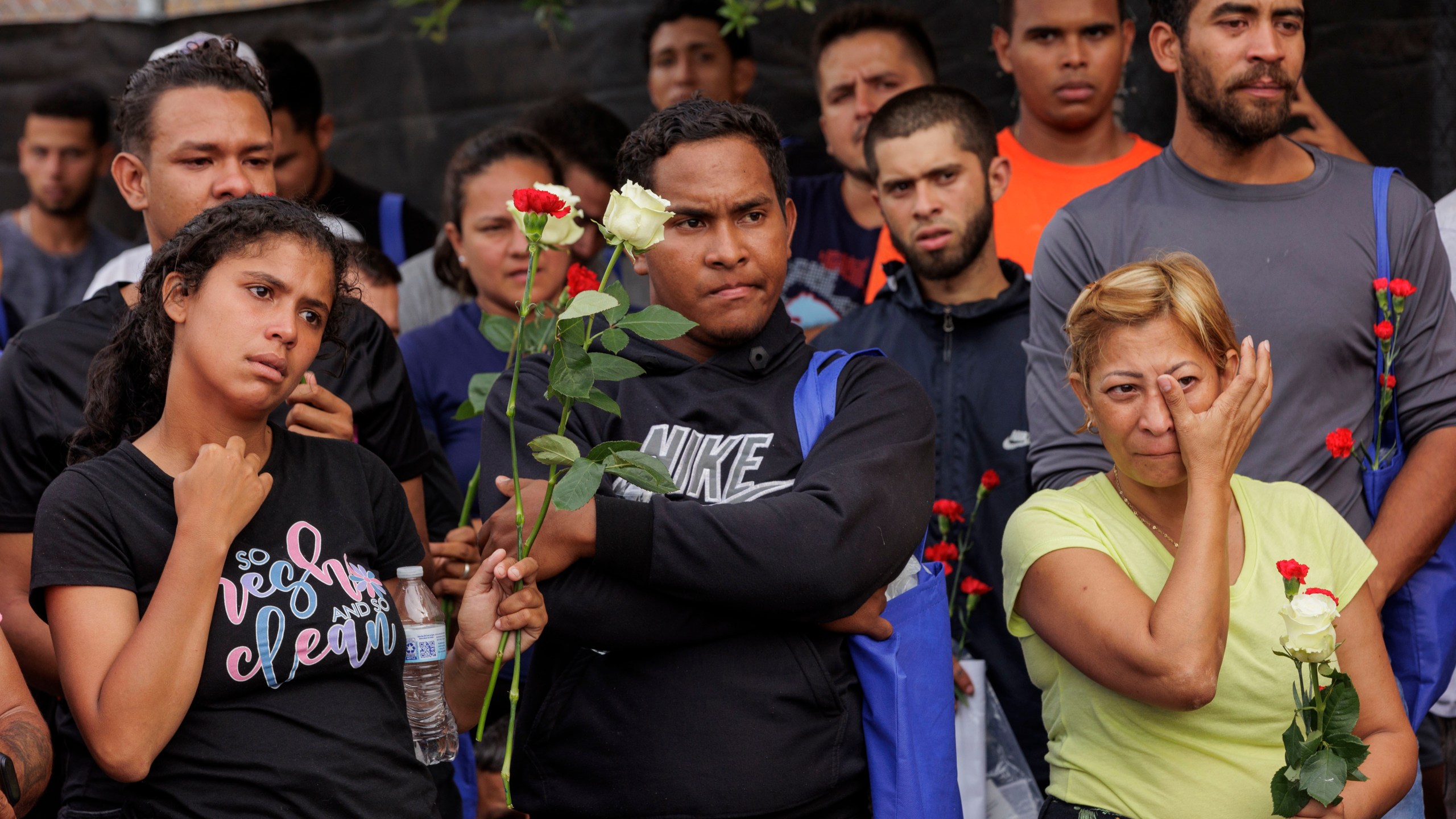 Migrants hold flowers and listen to speakers during a vigil for the eight migrants that were killed and several others that were injured the day before while waiting at a bus stop, in Brownsville, Texas, Monday, May 8, 2023. (AP Photo/Michael Gonzalez)