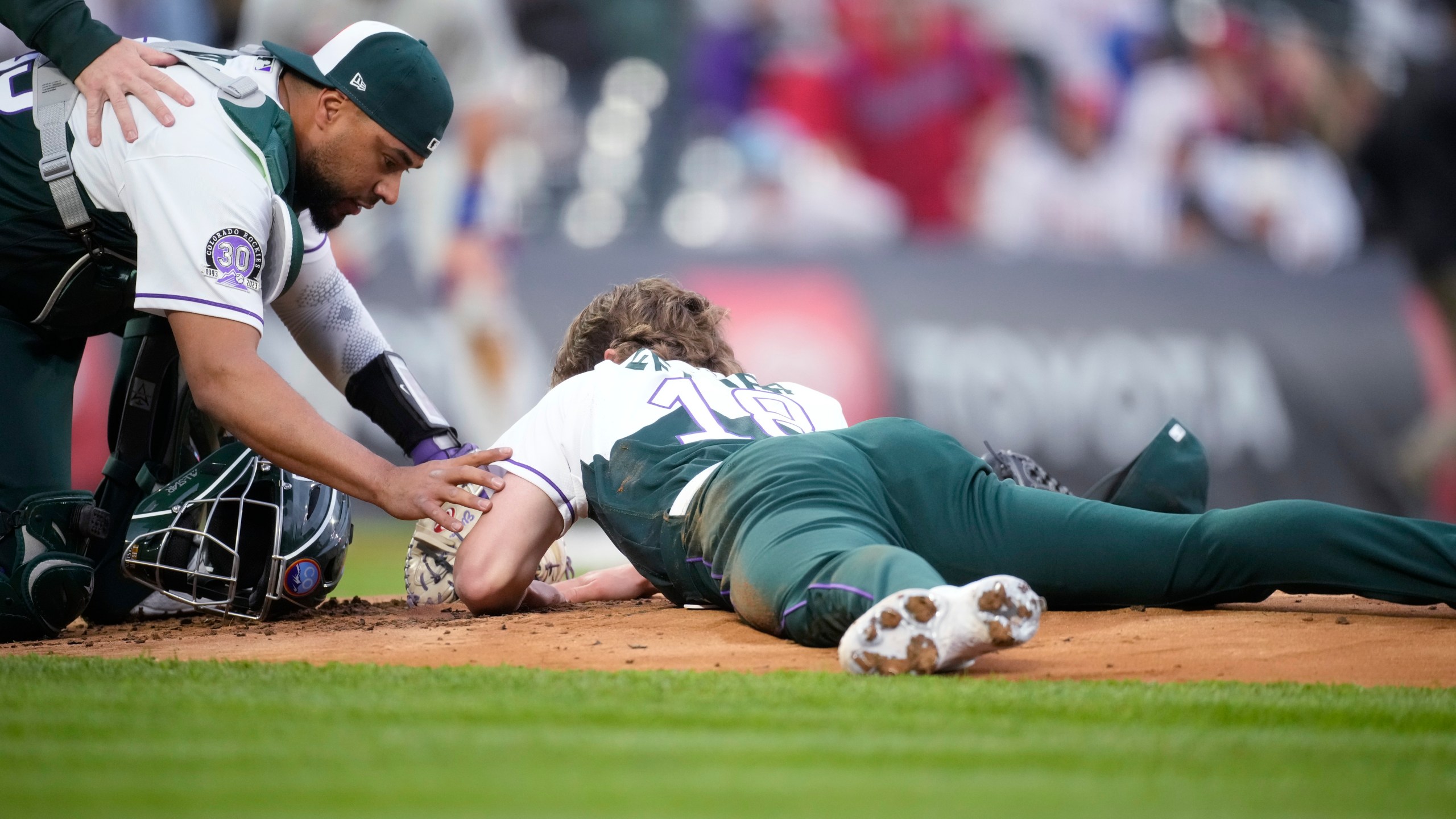 Colorado Rockies catcher Elias Diaz, left, checks on starting pitcher Ryan Feltner, who lies on the mound after getting hit by a single off the bat of Philadelphia Phillies' Nick Castellanos during the second inning of a baseball game Saturday, May 13, 2023, in Denver. (AP Photo/David Zalubowski)