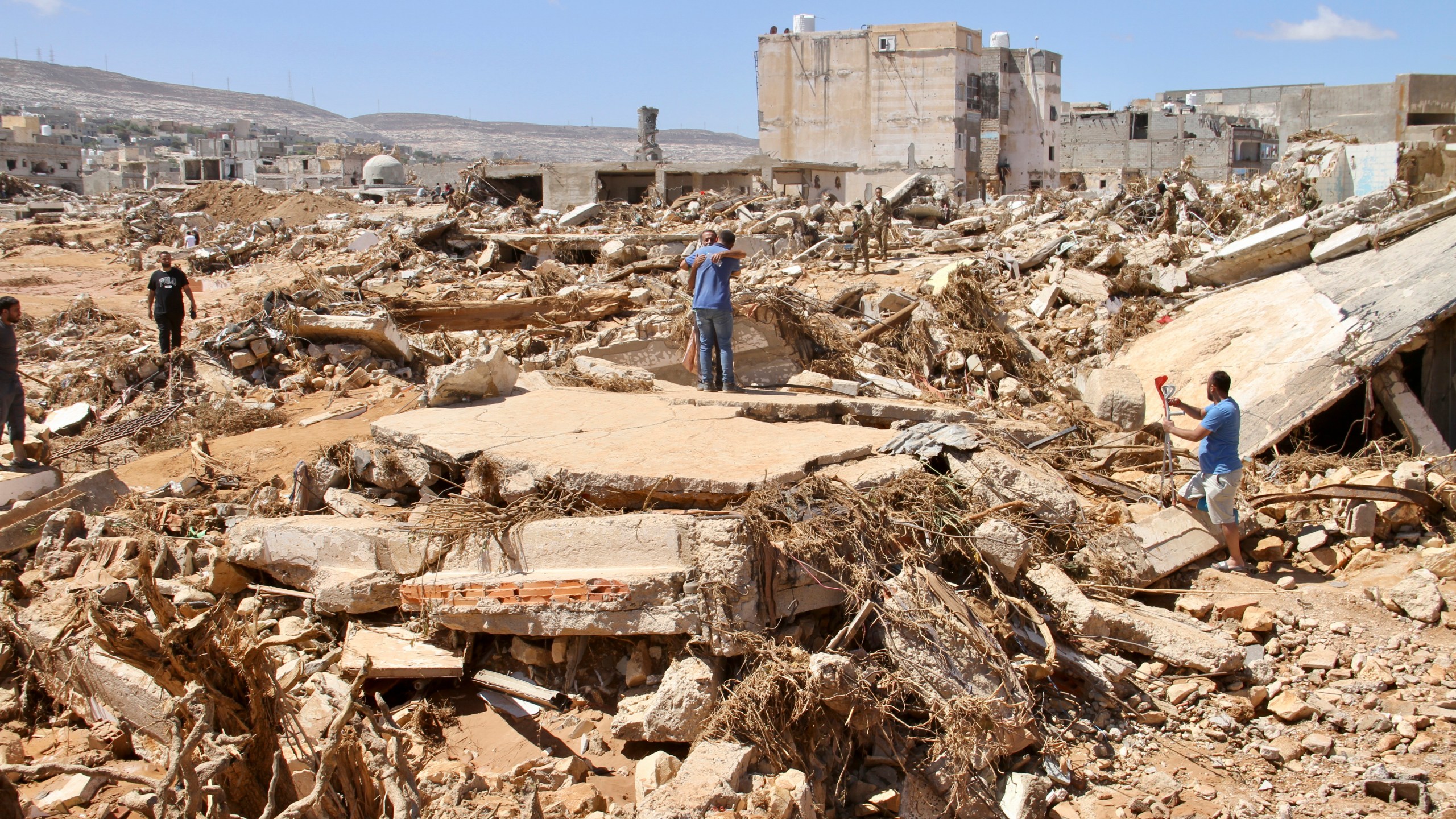 FILE - Two men hug as people look for survivors in the flooded city of Derna, Libya, Wednesday, Sept.13, 2023. For many Libyans, the disastrous flooding that killed more than 11,000 people have fostered a sense of unity. The collective grief has morphed into a rallying cry of national unity in a country blighted by 12 years of conflict and division. (AP Photo/Yousef Murad, File)