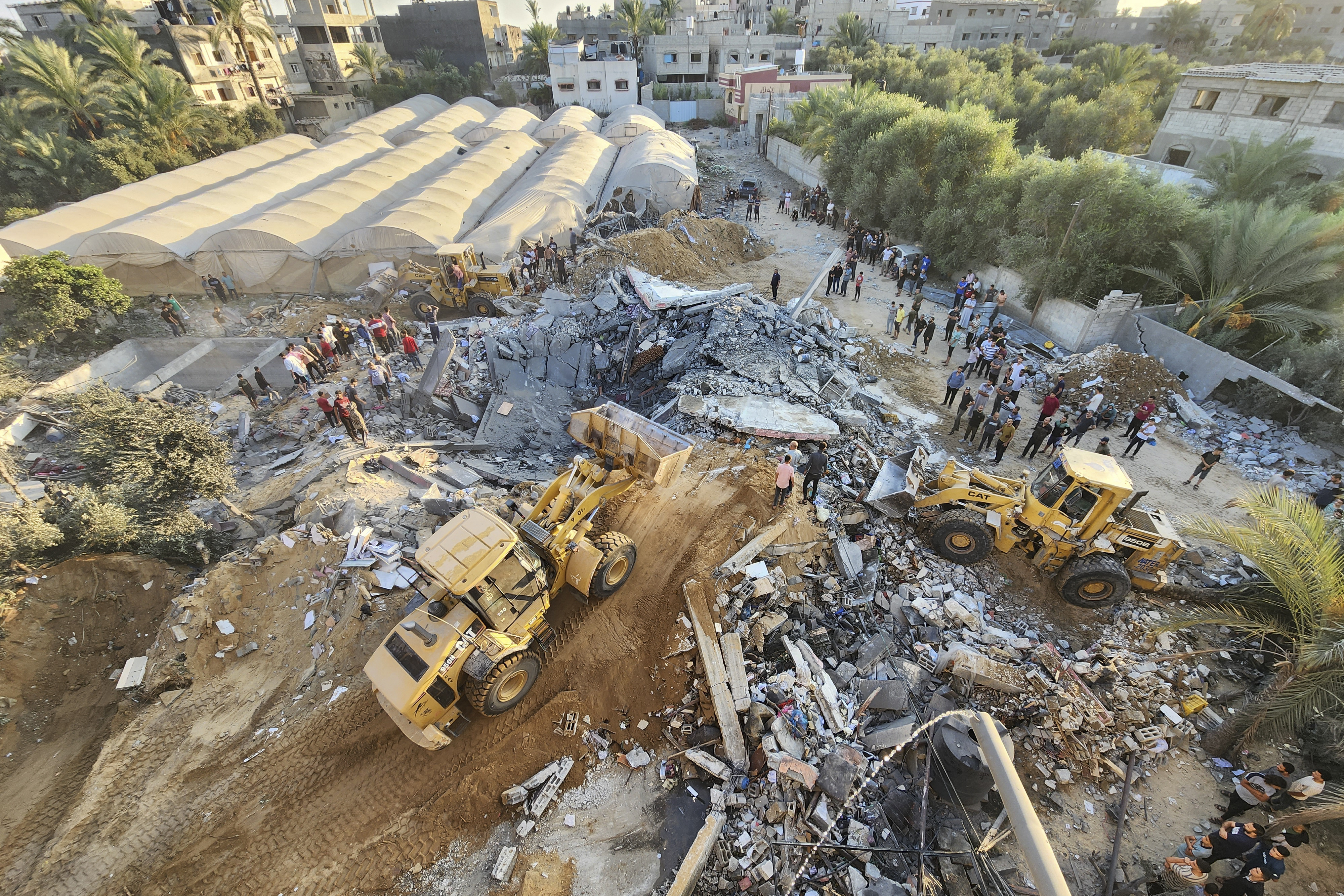 Palestinians stand by the rubble of a building destroyed in Israeli airstrikes in Deir el-Balah Gaza Strip, Sunday, Oct. 15, 2023. (AP Photo/Hasan Islayeh)