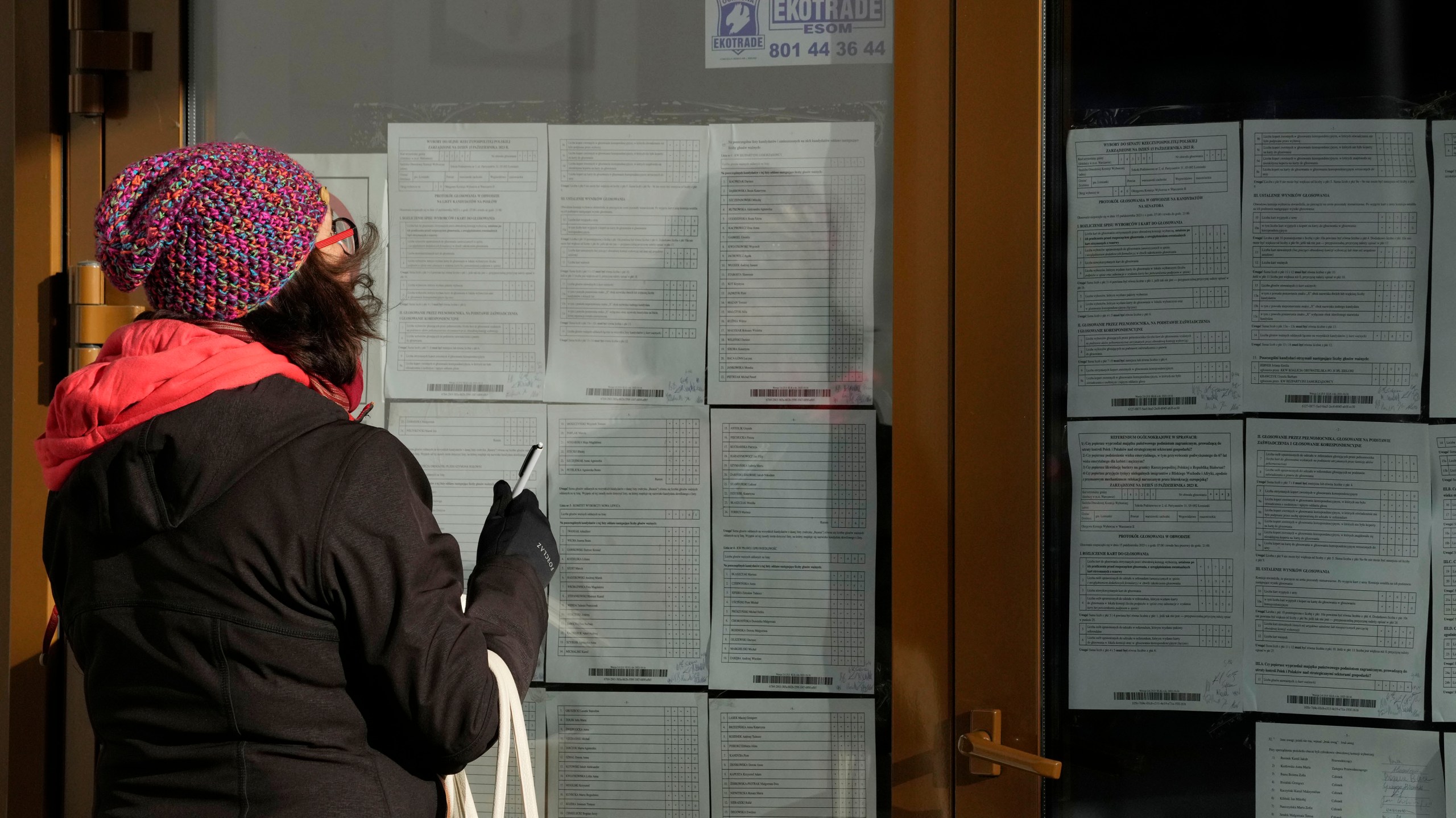 A woman is checking and taking photos of the results of Sunday's parliamentary elections, in which more than 73% of eligible voters took part of whom majority voted for opposition parties, in Lomianki, near Warsaw, Poland, Monday Oct. 16, 2023. The full official results are expected Tuesday, but exit polls say that people have grown tired of the ruling conservative and divisive Law and Justice party, PiS. (AP Photo/Czarek Sokolowski)