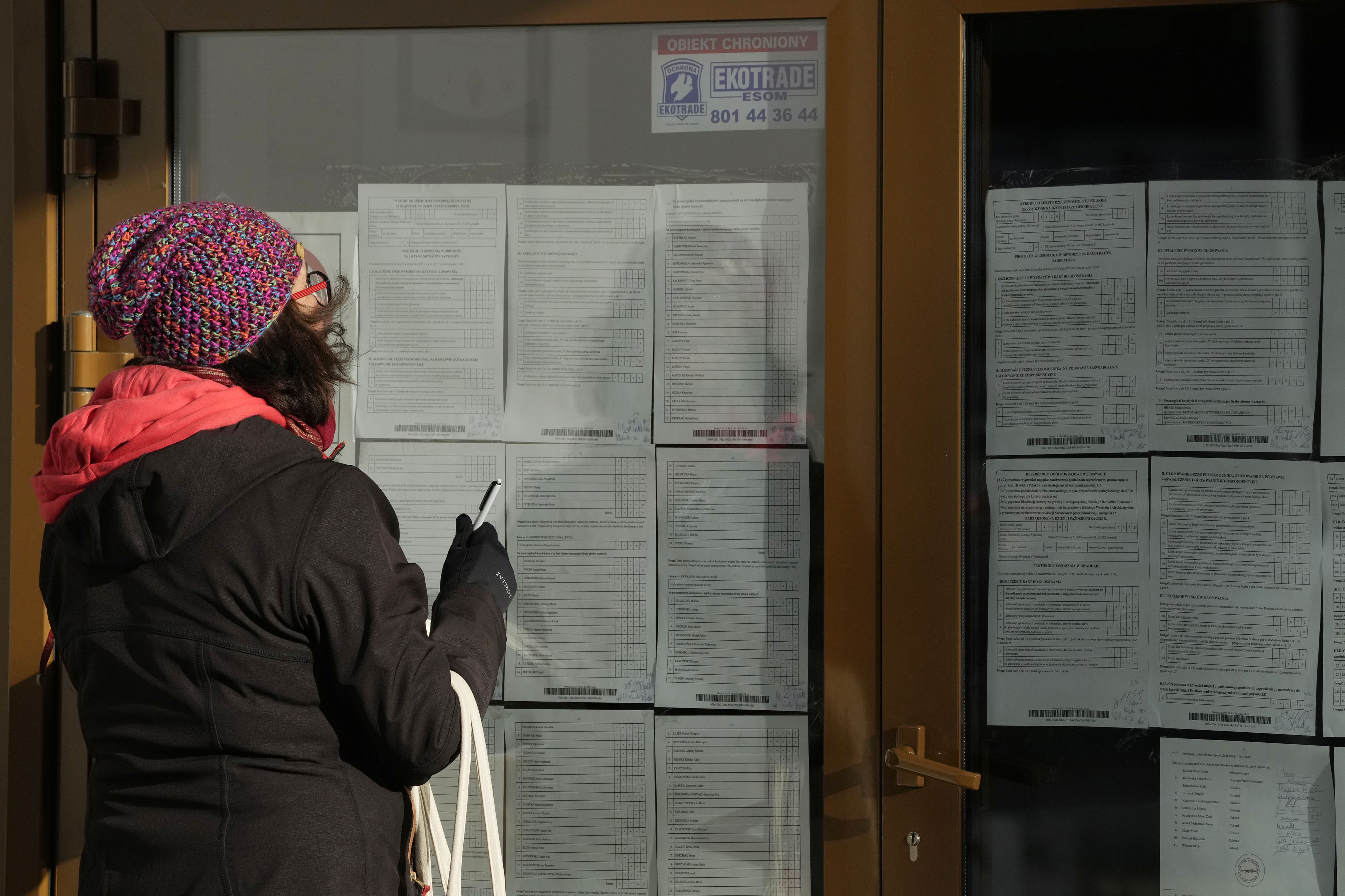 A woman is checking and taking photos of the results of Sunday's parliamentary elections, in which more than 73% of eligible voters took part of whom majority voted for opposition parties, in Lomianki, near Warsaw, Poland, Monday Oct. 16, 2023. The full official results are expected Tuesday, but exit polls say that people have grown tired of the ruling conservative and divisive Law and Justice party, PiS. (AP Photo/Czarek Sokolowski)