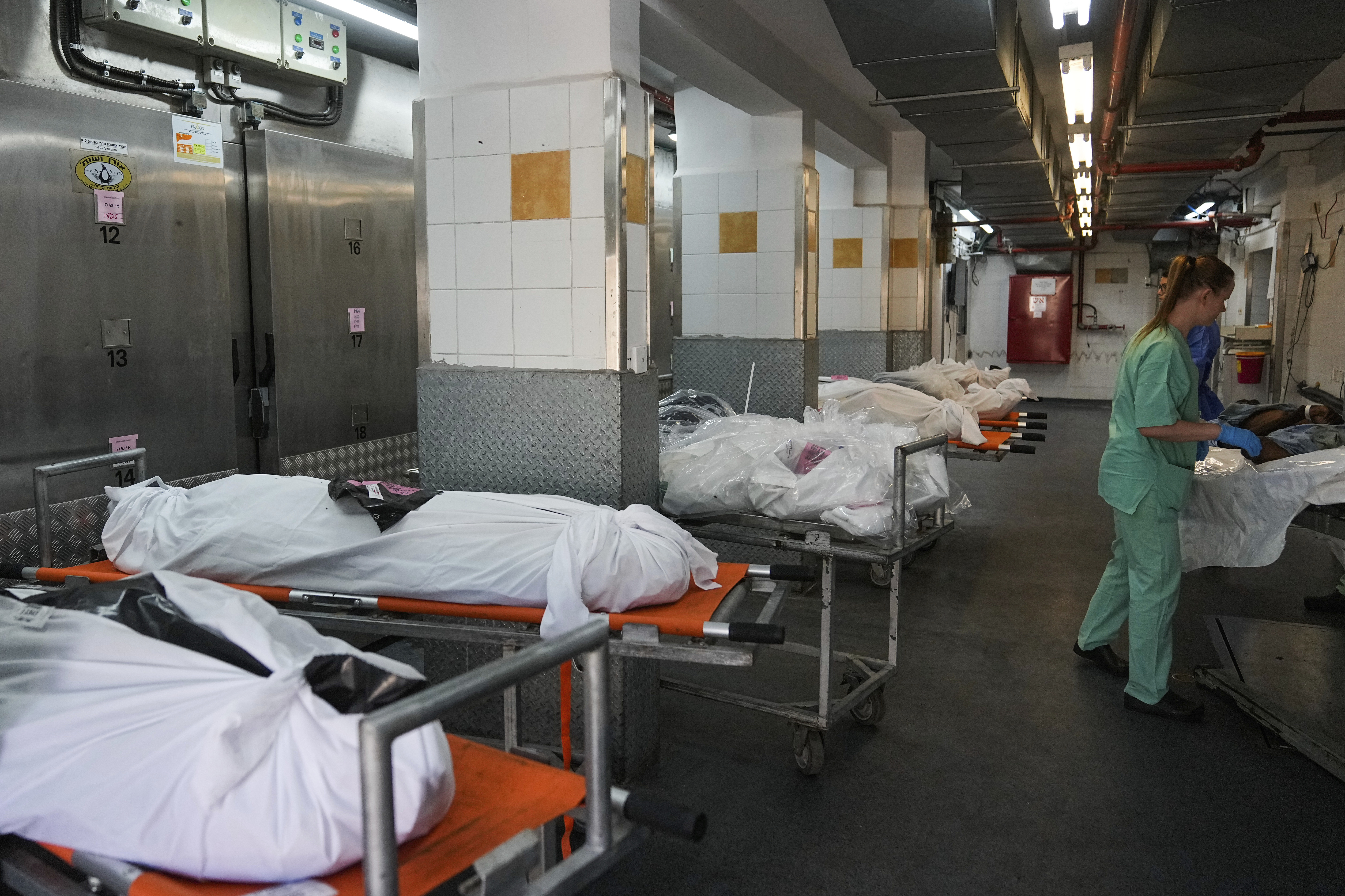 Forensic experts stand next to the bodies of Israelis killed by Hamas militants in the National Center for Forensic Medicine in Tel Aviv, Israel, Wednesday, Oct. 18, 2023. On Oct. 7, the militant Hamas rulers of the Gaza Strip carried out an unprecedented, multi-front attack on Israel, more than 1,400 people were killed and some 200 captured. (AP Photo/Ohad Zwigenberg)