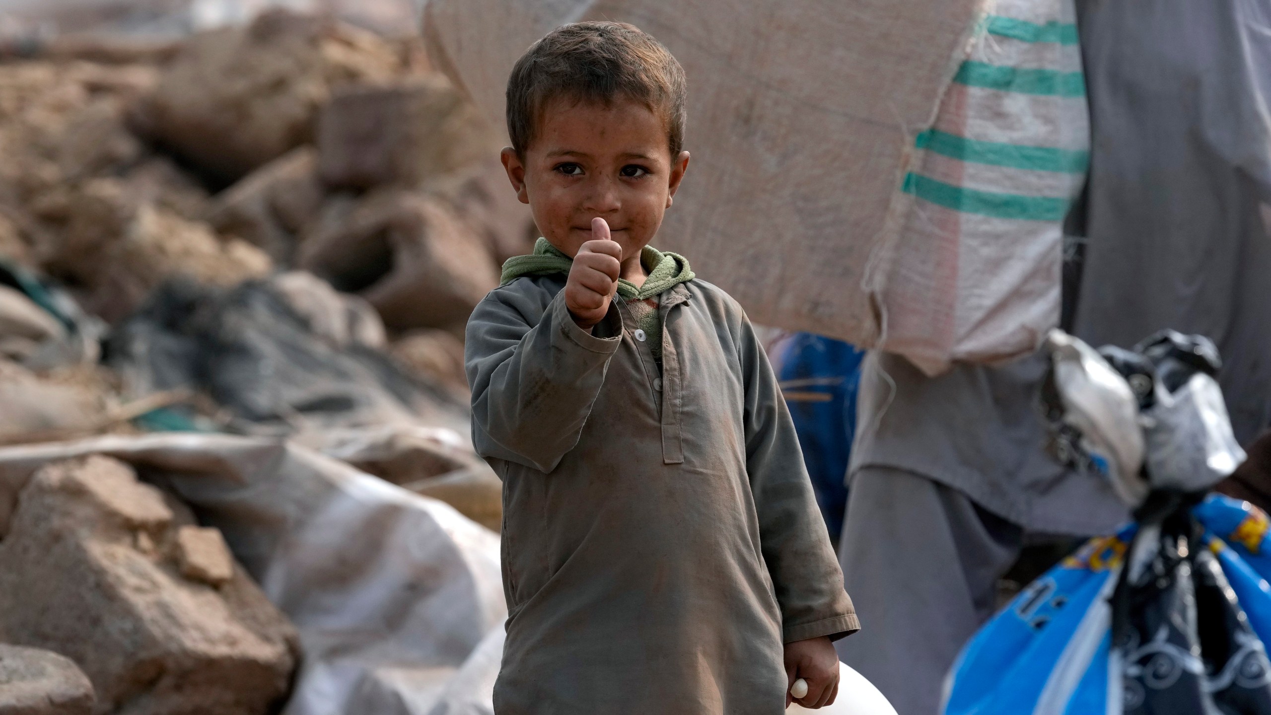 An Afghan boy gestures as he stands beside his family's belongings retrieved from their damage mud homes demolished by authorities during a crackdown against an illegal settlement and immigrants, on the outskirts of Islamabad, Pakistan, Wednesday, Nov. 1, 2023. (AP Photo/Anjum Naveed)