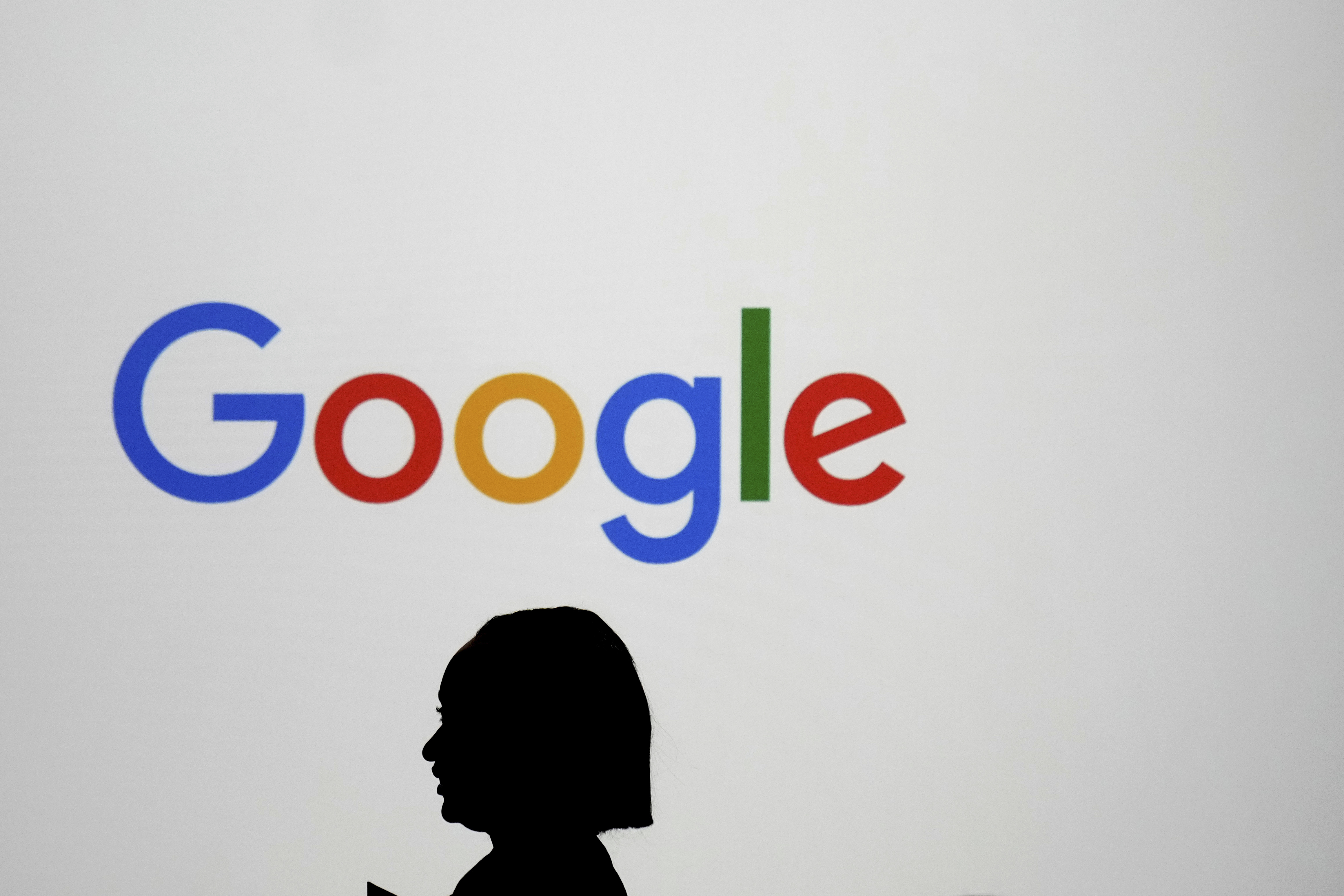 FILE - A woman walks by a giant screen with a logo at an event at the Paris Google Lab on the sidelines of the AI Action Summit in Paris, Sunday, Feb. 9, 2025. (AP Photo/Thibault Camus, File)